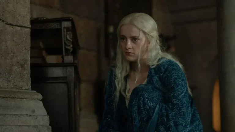 Phia Saban as Helaena Targaryen wearing a teal dress and crouching in a dimly lit stone room in House of the Dragon.