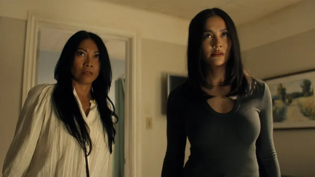 Anggun as Amisha and Agnez Mo as Lila Hoth looking upwards with serious expressions indoors in Reacher Season 4.