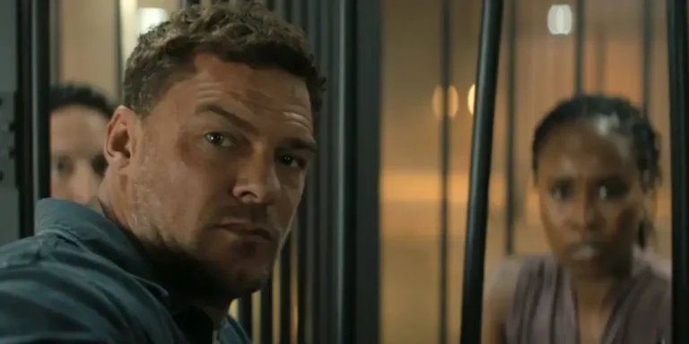Jack Reacher, a muscular man with short brown hair and a furrowed brow, stares intensely forward through vertical metal bars.